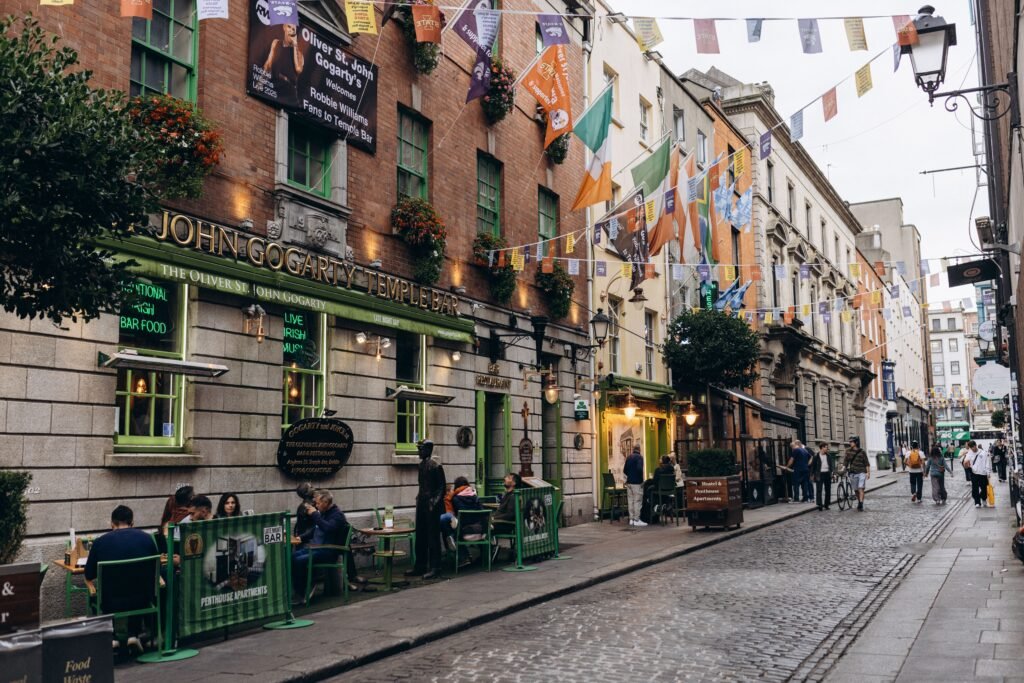 Pasaporte abierto con sello de entrada a Irlanda junto a billetes de avión y una maleta sobre una mesa de madera.