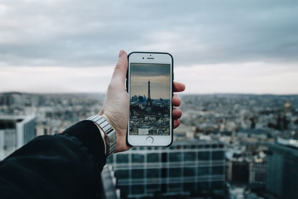 Mano sosteniendo un teléfono móvil que muestra en la pantalla la Torre Eiffel con la auténtica Torre Eiffel de fondo en París.